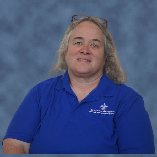 A person wearing a blue polo shirt with "Scouting America" text and a logo, smiling, glasses on their head.